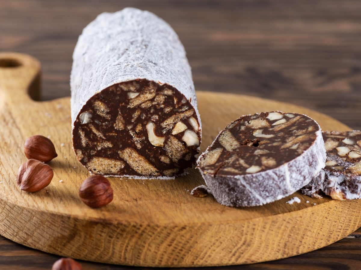 Frontalansicht auf eine angeschnittene Schokosalami auf einem Holzbrett.