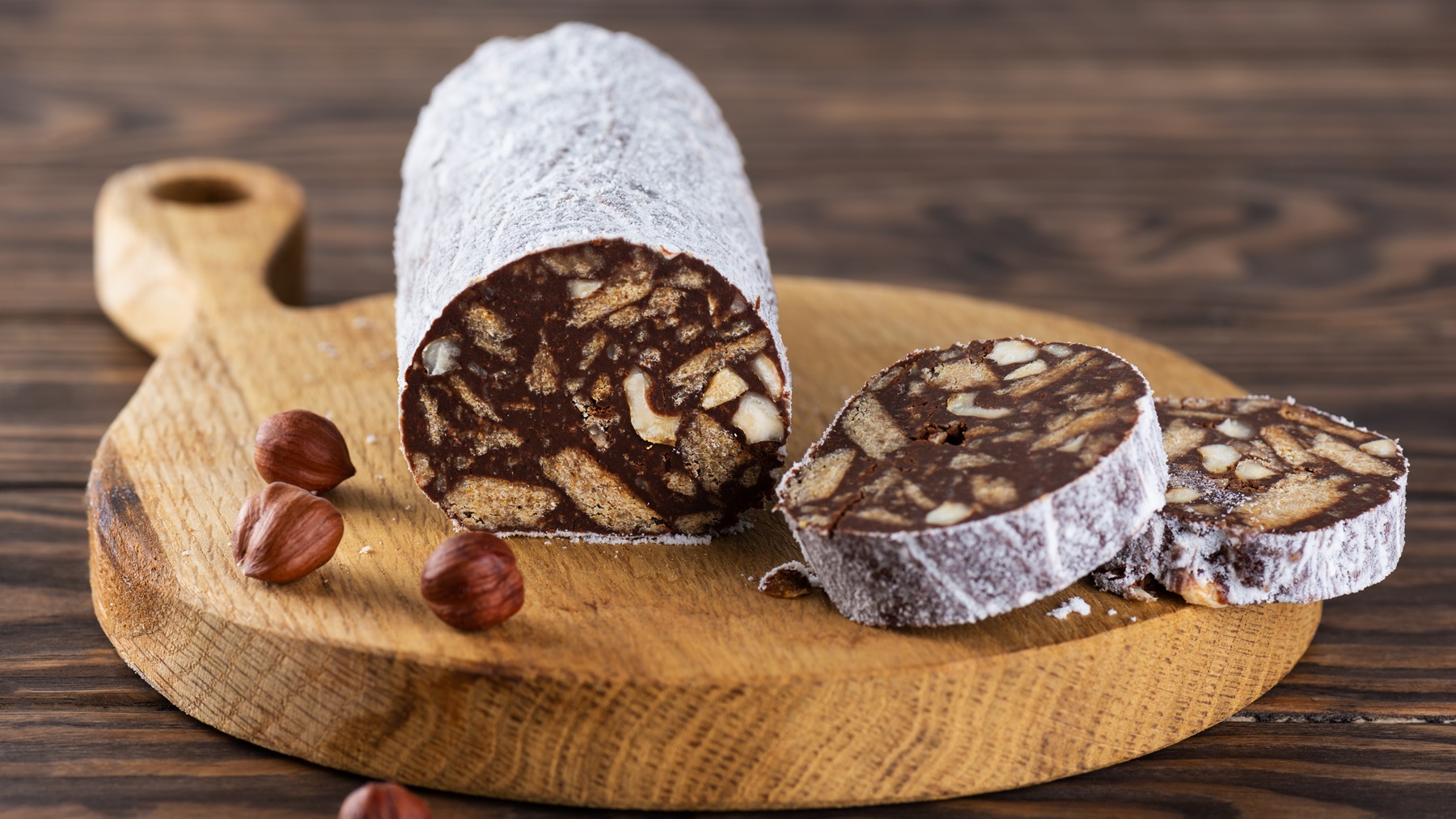 Frontalansicht auf eine angeschnittene Schokosalami auf einem Holzbrett.