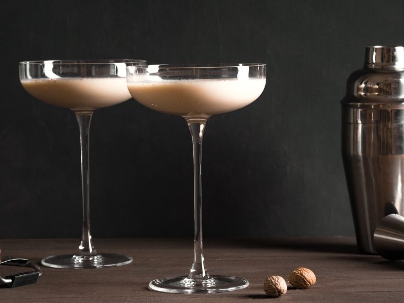 Zwei Martini-Gläser mit Tahini Martini, daneben ein Shaker und frische Tonkabohnen.