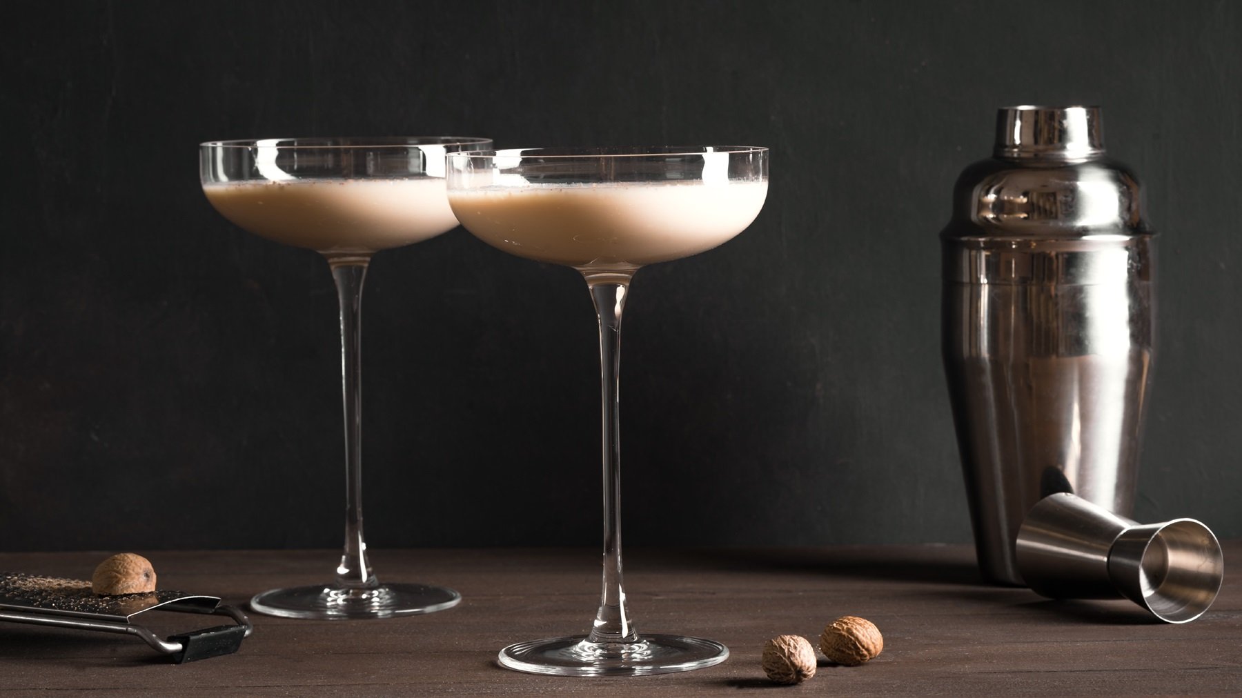 Zwei Martini-Gläser mit Tahini Martini, daneben ein Shaker und frische Tonkabohnen.