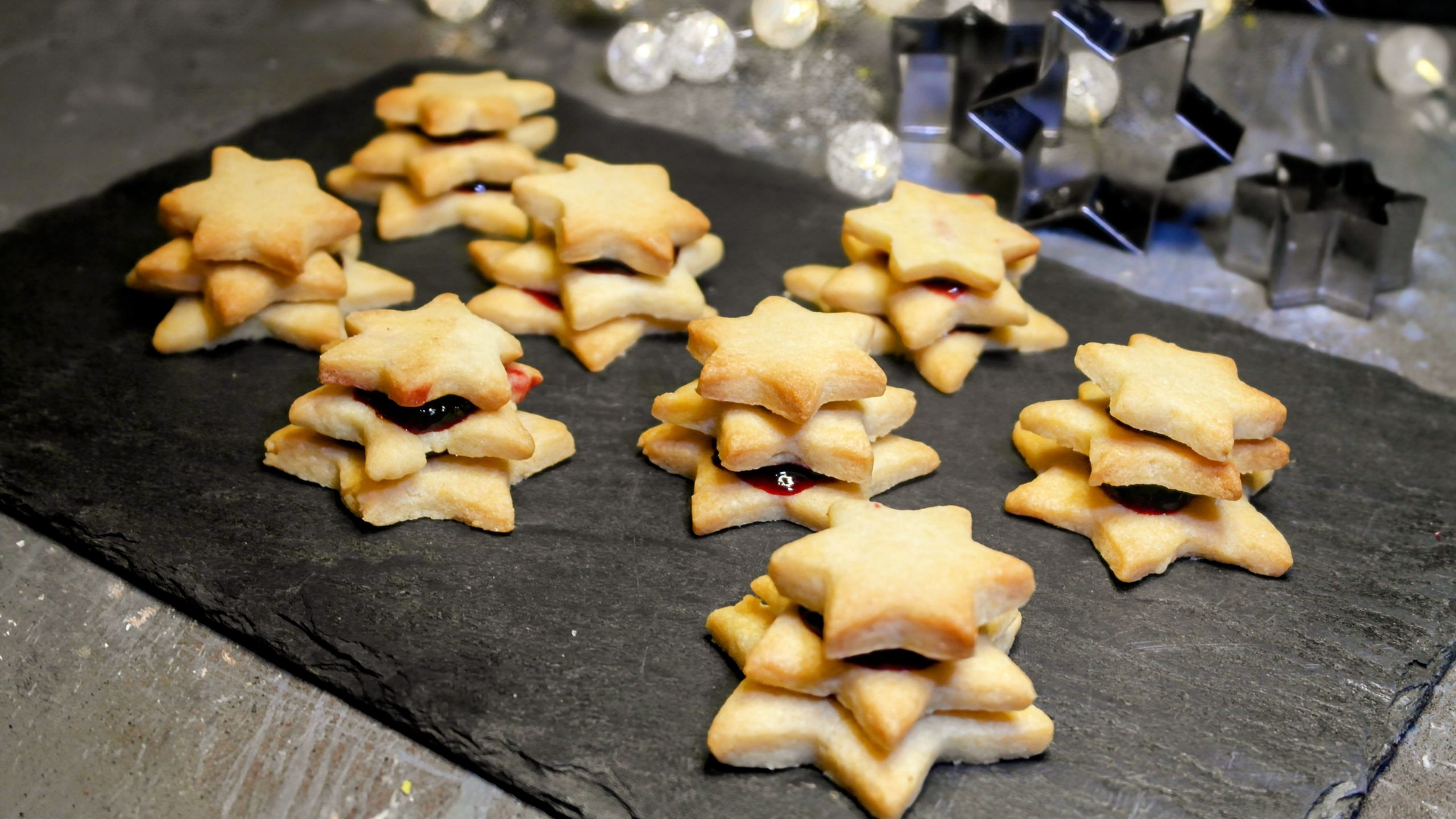 Mehrere Terrassen-Plätzchen auf einer schwarzen Schieferplatte von schräg oben fotografiert. Im Hintergrund weihnachtliche Dekoration.