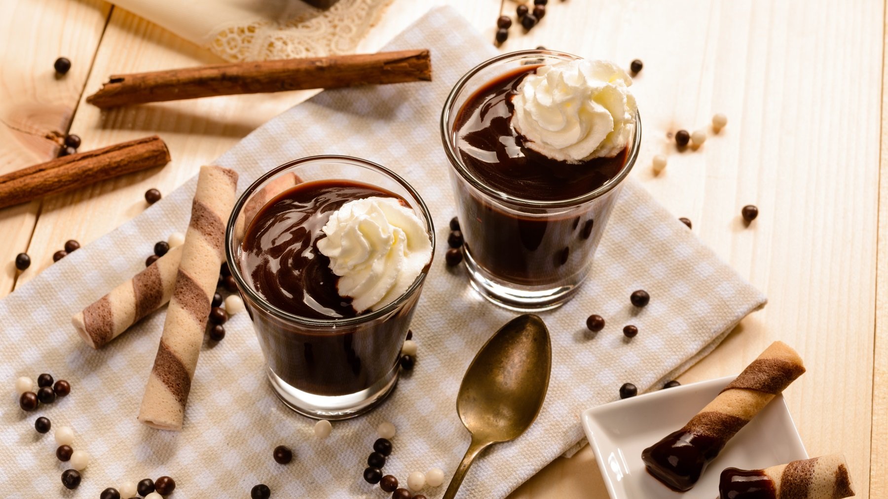 Draufsicht auf zwei Gläser mit cioccolata calda, mit Schlagsahnehäubbchen, daneben Schokoperlen und Plätzchen.