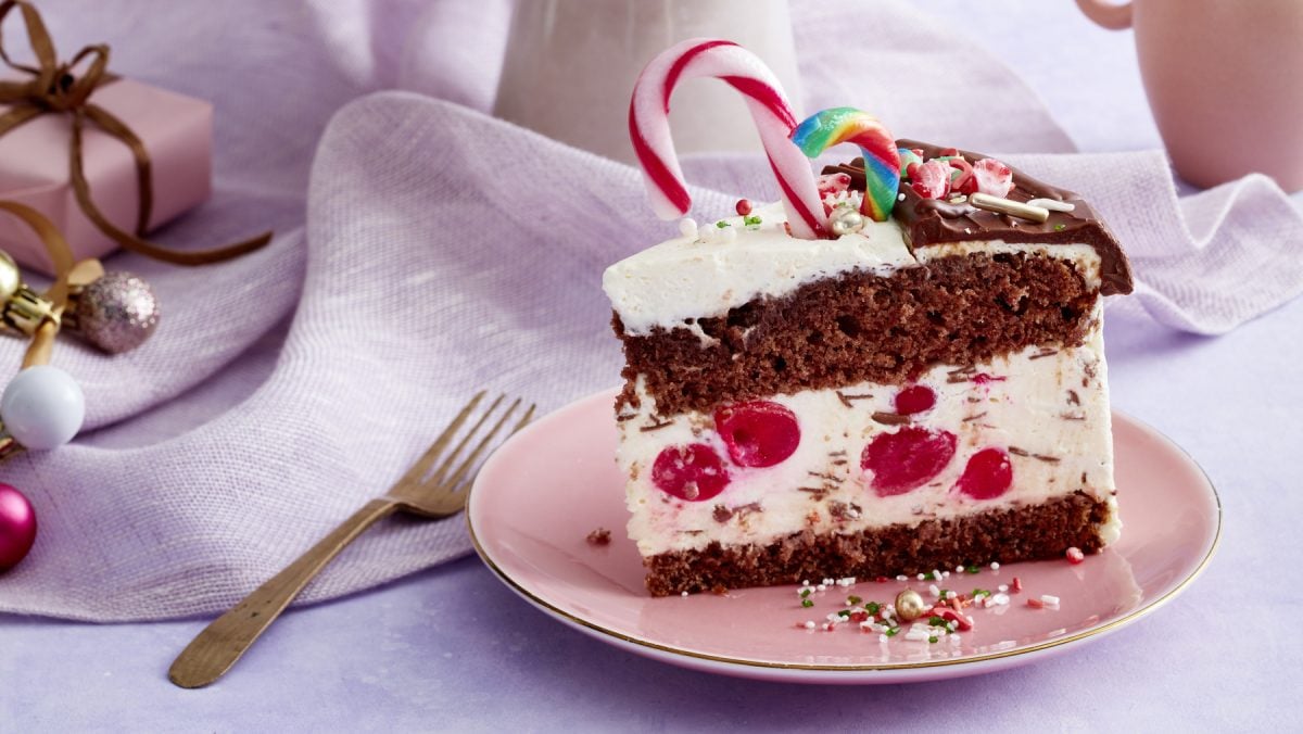 Ein Stück festliche Kirsch-Schmand-Torte mit Zuckerstangen drauf auf einem Teller mit hellem, festlichen Hintergrund.