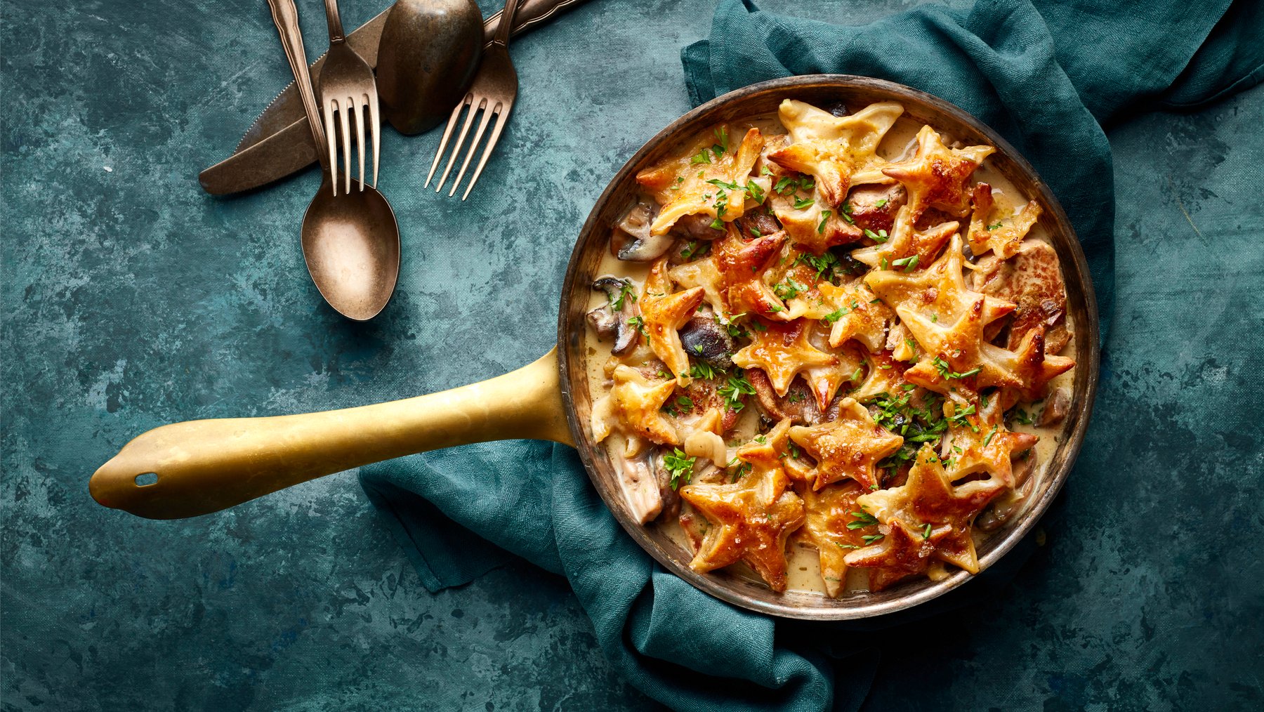 Draufsicht: Gebackenes Filettöpfchen mit Sternenhaube; Pfanne mit Fleisch und Pilzen in heller Sauce und gebackenen Blätterteig-Sternen darauf.