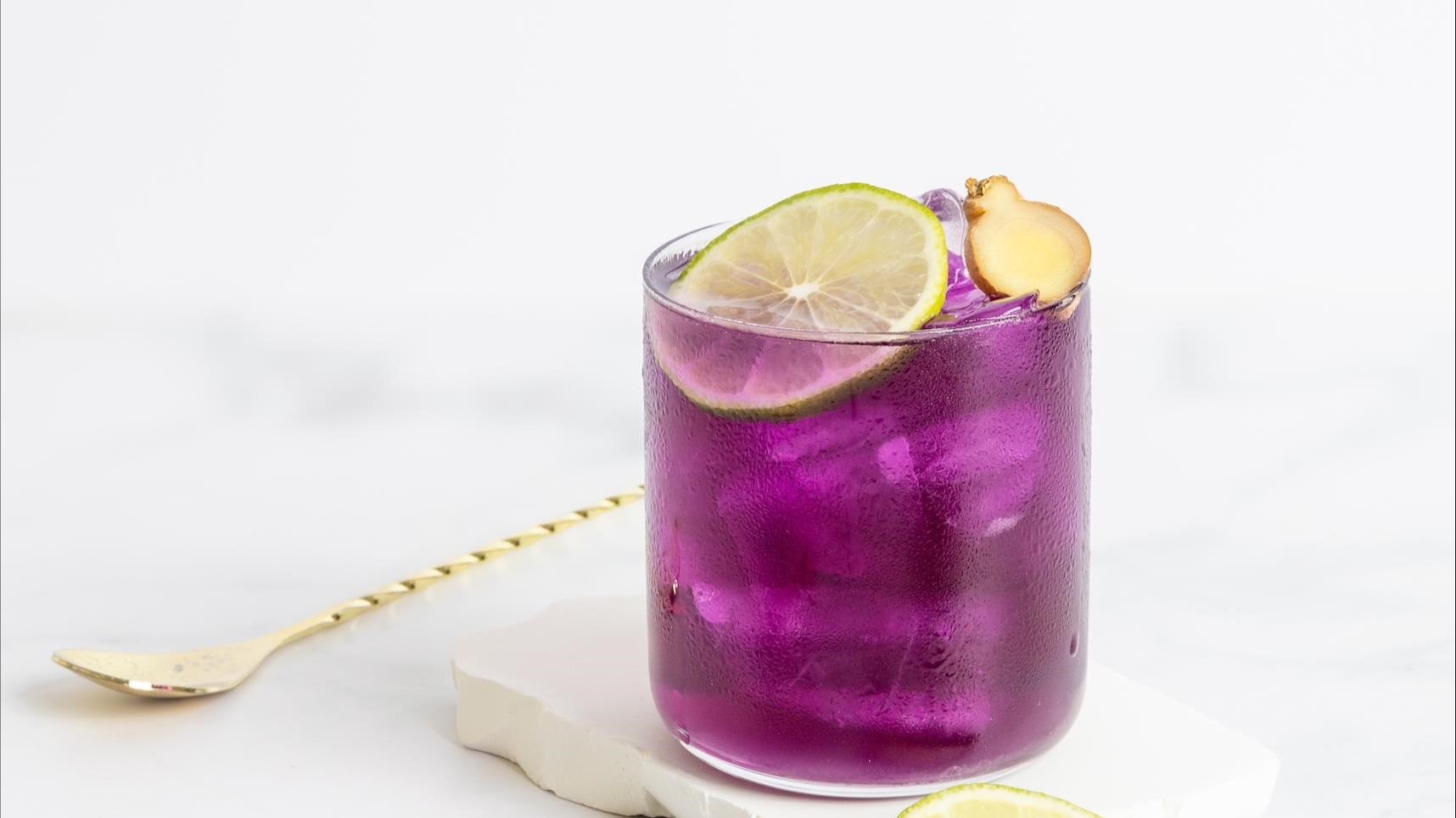 Frontalansicht auf ein Glas mit einem violetten Lavender Mule, daneben ein Barlöffel.