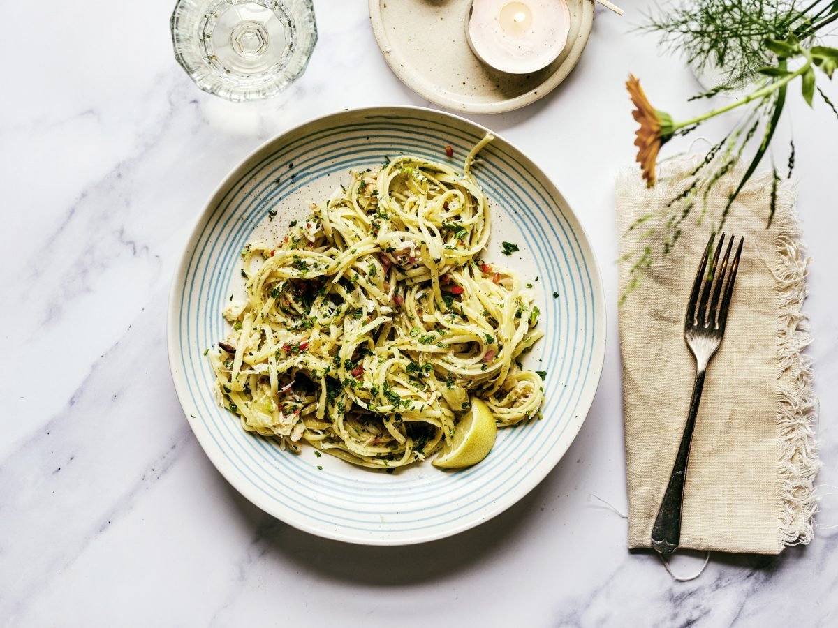 Ein heller Teller mit der Pasta auf einem weißen Marmortisch, der eingedeckt ist mit stilvollem Geschirr. Alles direkt von oben fotografiert.