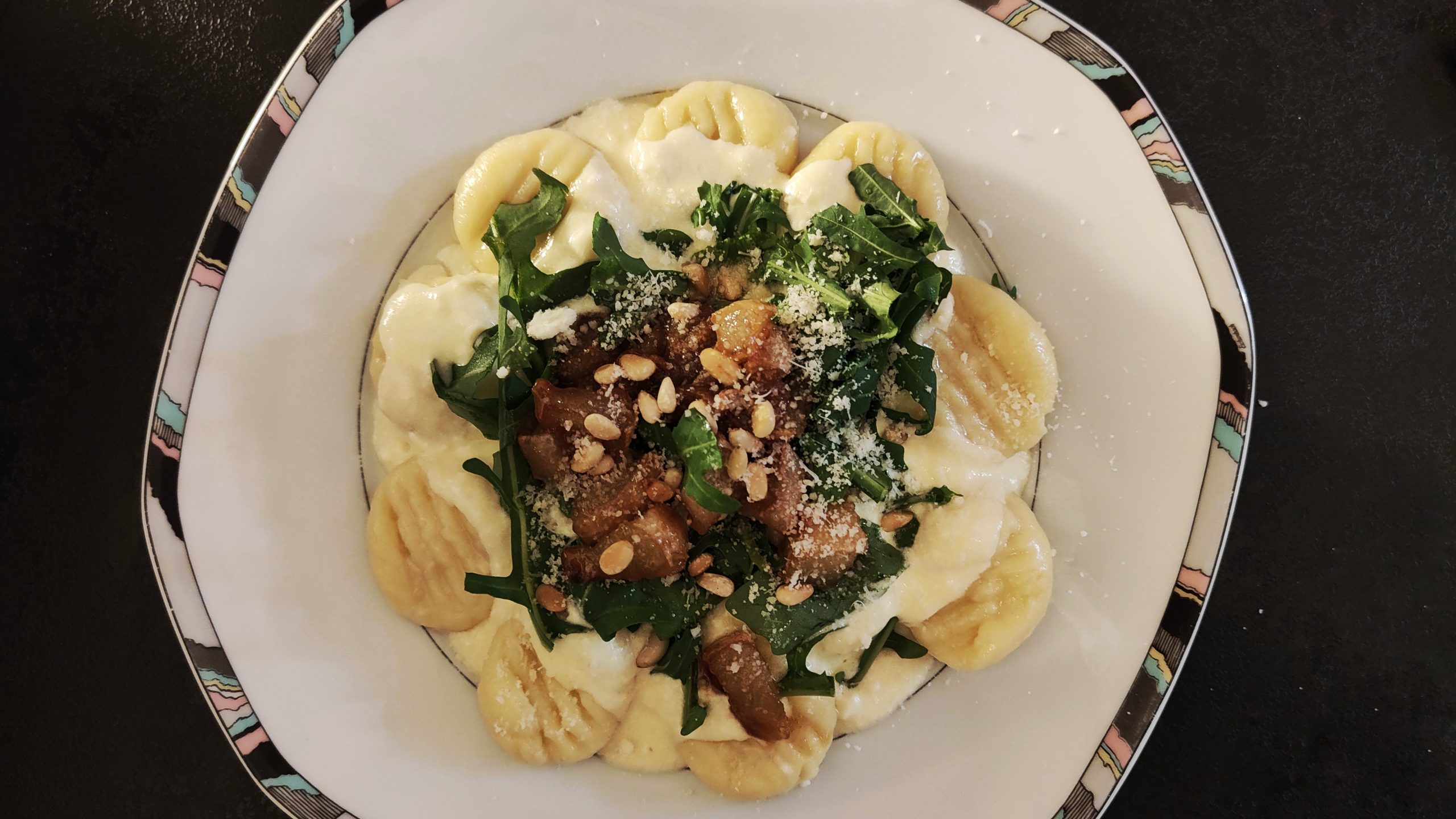 Gnocchi in cremiger Provolone-Sauce, garniert mit Rucola, karamellisierter Birne, Pinienkernen und Parmesan, angerichtet auf elegantem Porzellanteller.