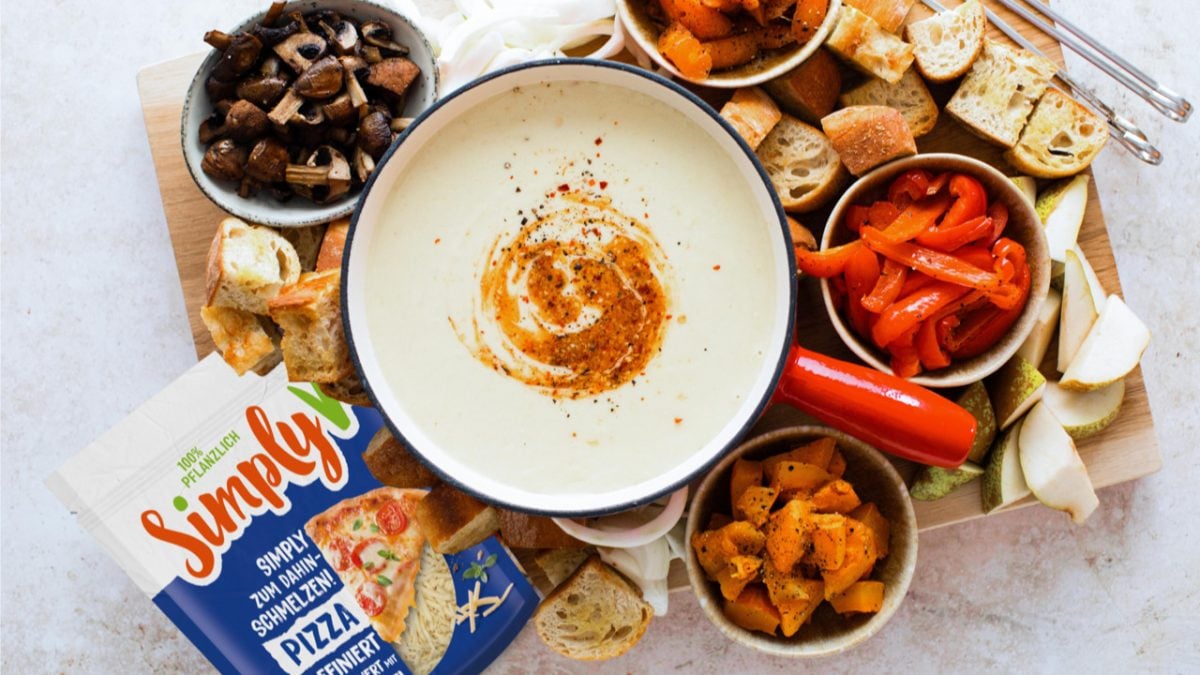 Drauf sicht auf pflanzliches Käsefondue, daneben Ofengemüse, Baguette und Birnen sowie Simply-V-Verpackung.