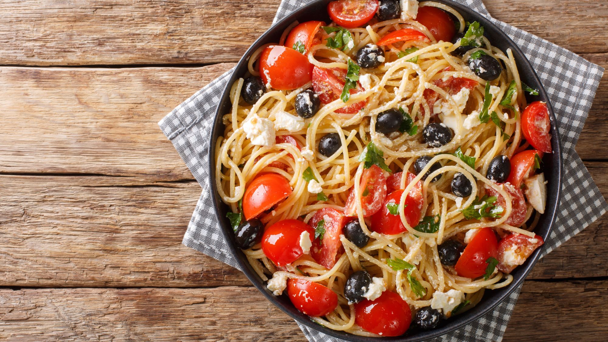 Pasta al greco mit schwarzen Oliven, Kirschtomaten, Fetakäse und frischen Kräutern in einer rustikalen Schale.