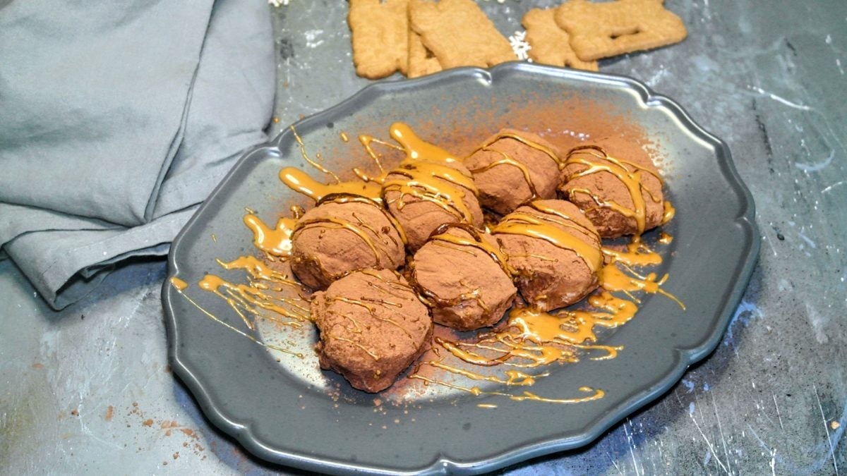 Ein grauer Teller mit den Tiramisu Bällchen auf einem grauen Steintisch mit Spekulatius im Hintergrund. Links daneben ein graues Tuch.