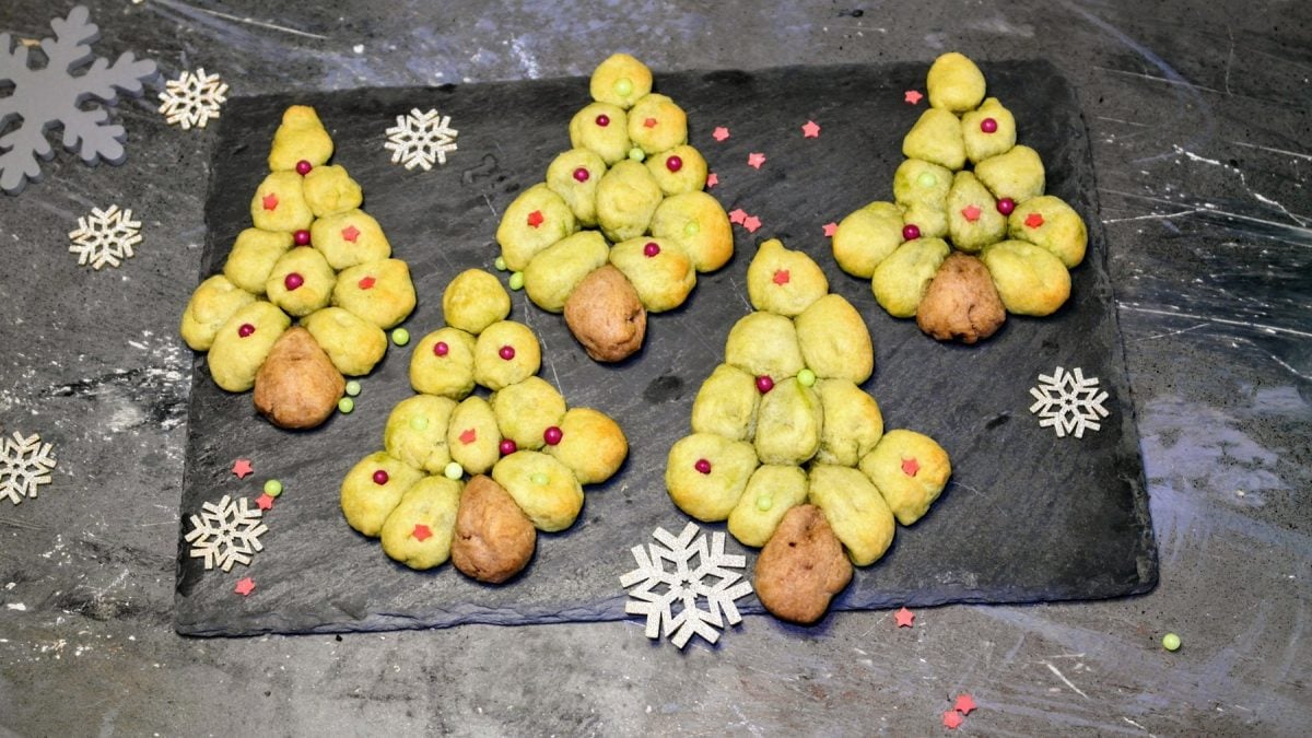 Ein eschwarze Schieferplatte mit den Cookies auf einem grauen Tisch mit weihnachtlicher Deko. Alles direkt von oben fotografiert.