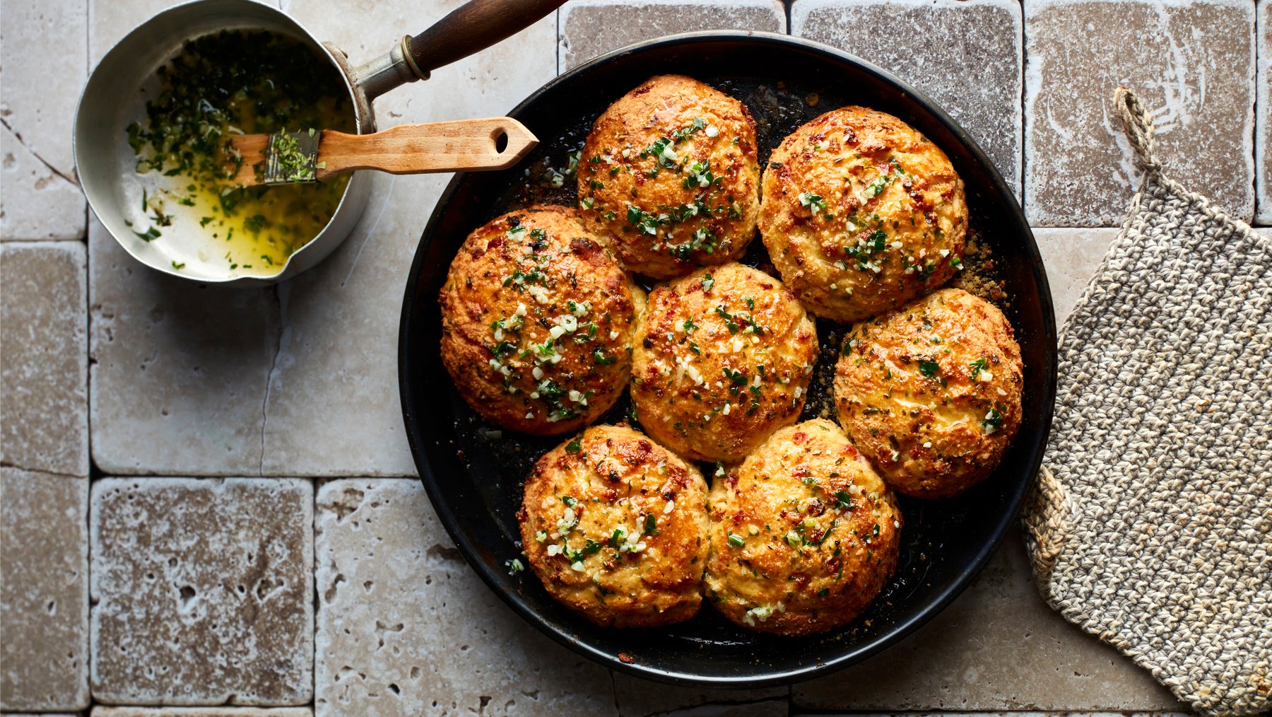 Draufsicht: Triple-Cheese-Brötchen aus der Pfanne, daneben Knoblauchbutter mit Pinsel.