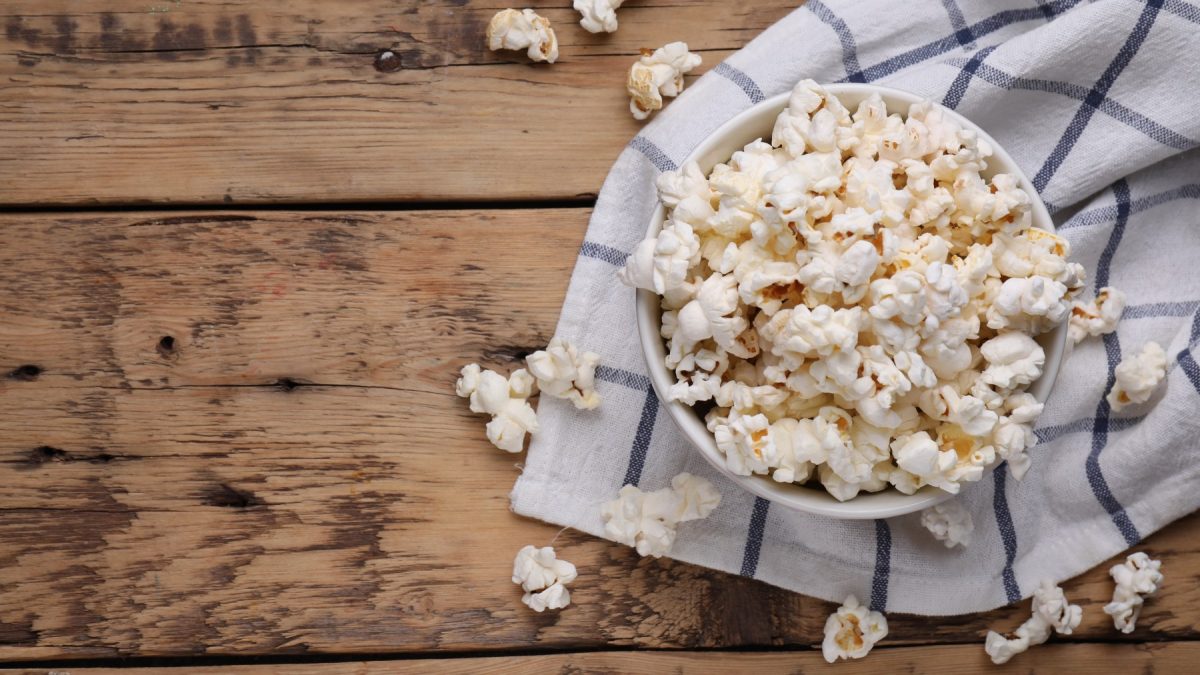 Trüffelpopcorn in einer weißen Schüssel auf einem Geschirrtuch auf hölzernem Hintergrund.