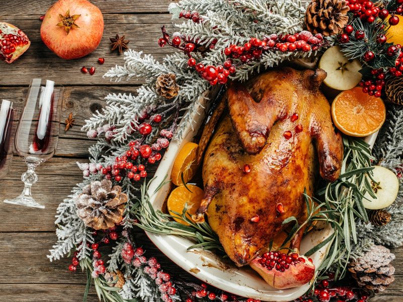 Gebratene Weihnachtsente in einer Keramikform, dekoriert mit Granatapfelkernen, Tannenzweigen, Orangenscheiben und festlichen Beeren.