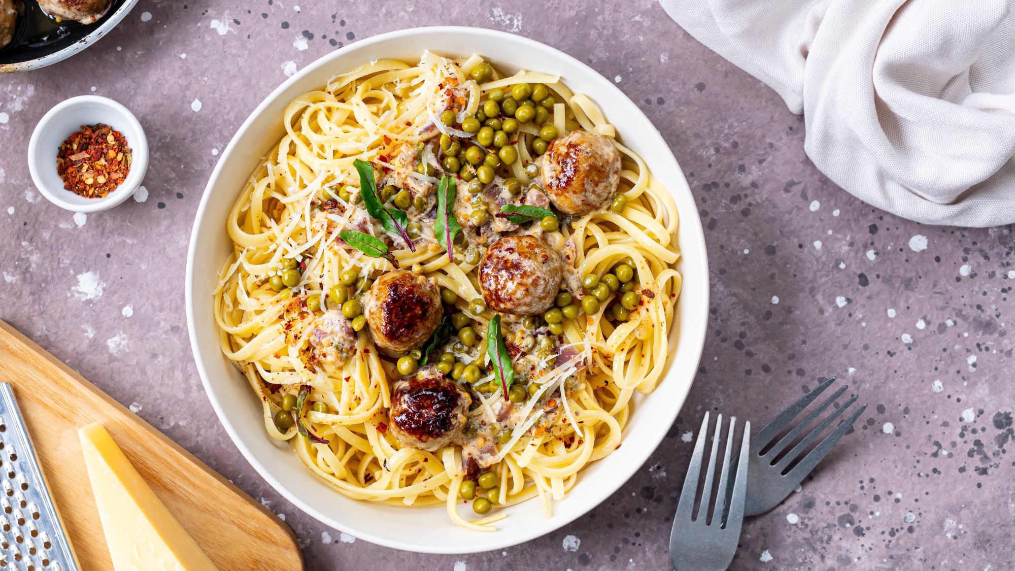 Wikinger-Pasta mit Fleischbällchen, grünen Erbsen, frischen Kräutern und geriebenem Parmesan, angerichtet in einer weißen Schale.