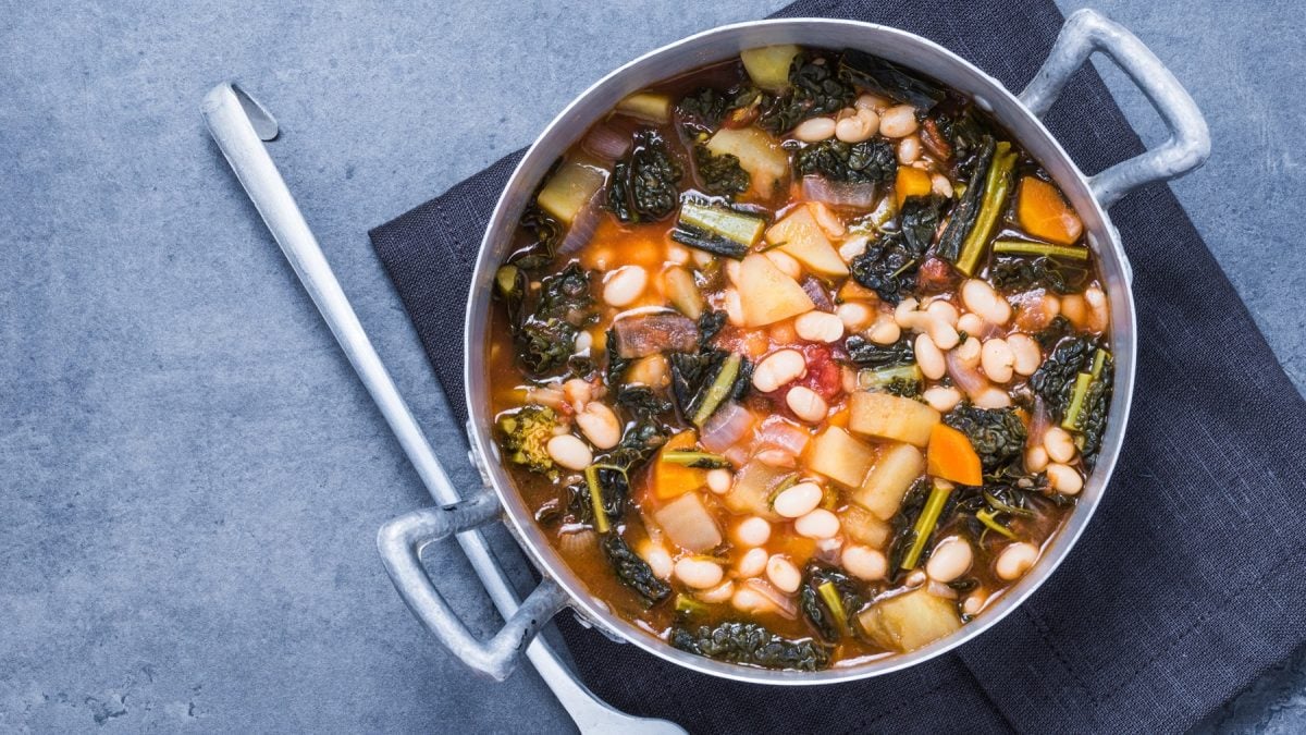 Ein silberner Topf mit der Wirsingsuppe auf einem grauen Tisch direkt von oben fotografiert.