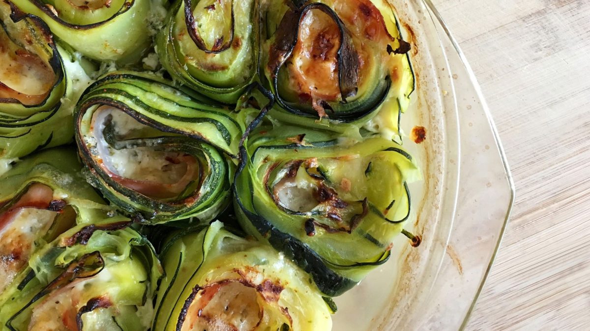 Zucchini-Röllchen gefüllt mit Käse und Schinken, überbacken mit Käse in einer runden, gläsernen Auflaufform.