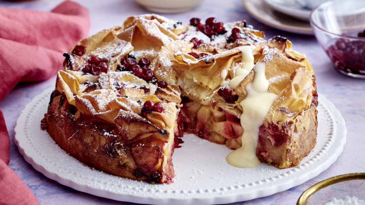 Angeschnittene Apfel-Strudel-Torte mit Vanillesauce auf Servierteller.