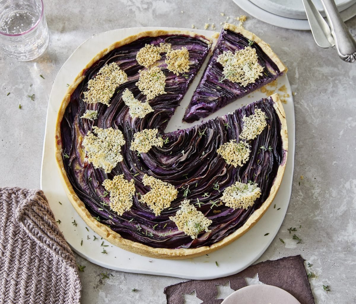 Die violette Möhren-Tarte mit Parmesanchips auf einem weißen Teller und grau-steinernem Untergrund. Alles direkt von oben fotografiert.