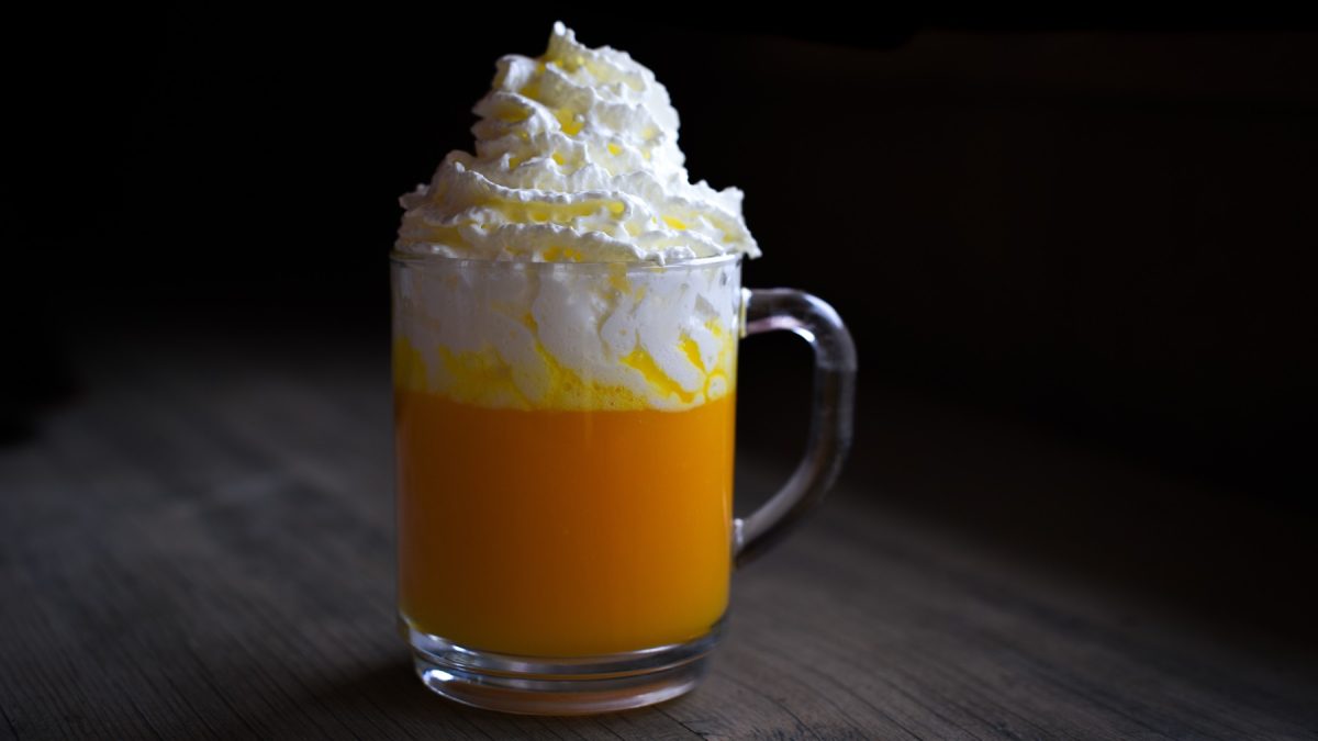 Ein Glas mit dem Bombardino auf einem dunklen Holztisch mit schwarzem Hintergrund. Alles sehr nah und recht zentral fotografiert.