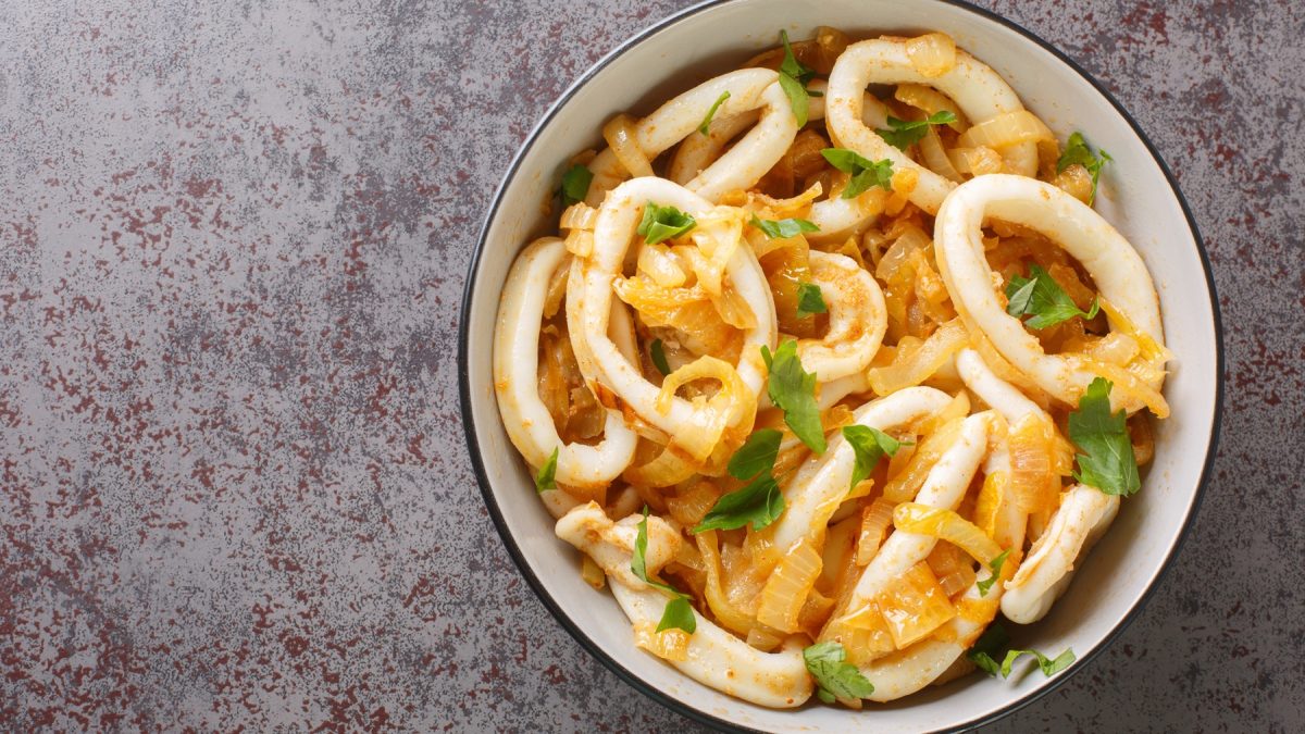 Draufsicht auf eine wei0ße Schüssel mit Calamares encebollados vor einem grauen Untergrund.