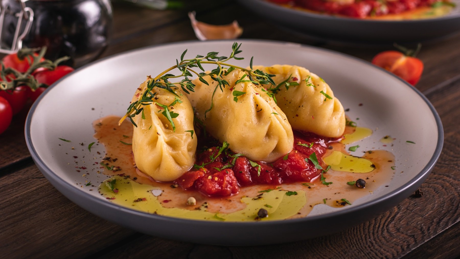 Ein grauer Teller mit den Teigtaschen und Tomatensauce auf einem Holztisch von schräg oben fotografiert.