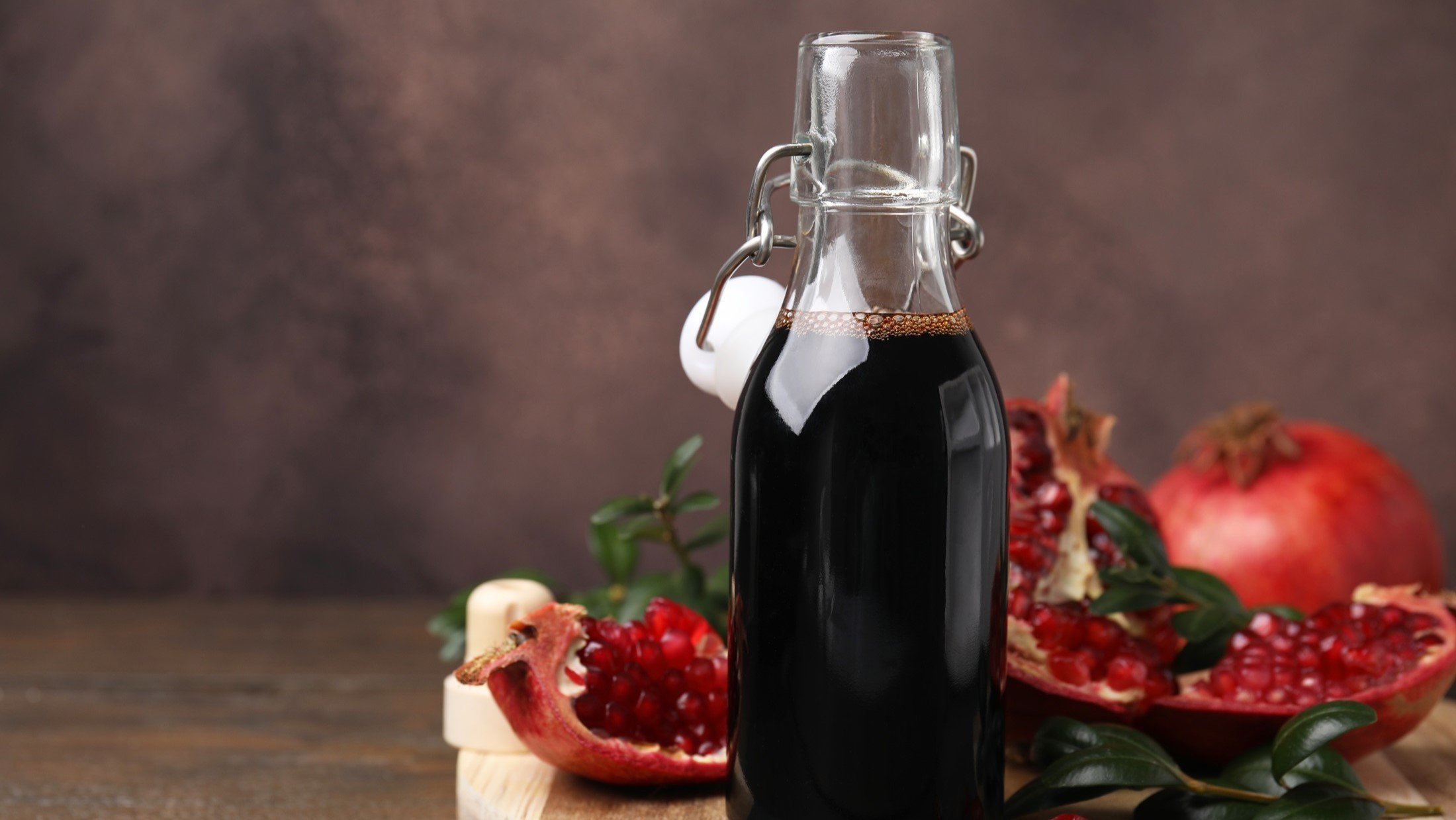 Frontal: Eine Flasche mit einem selbst gemachten Balsamico-Dressing mit Granatapfel vor einem dunklen Hintergrund. Daneben liegen Teile eines Granatapfels.