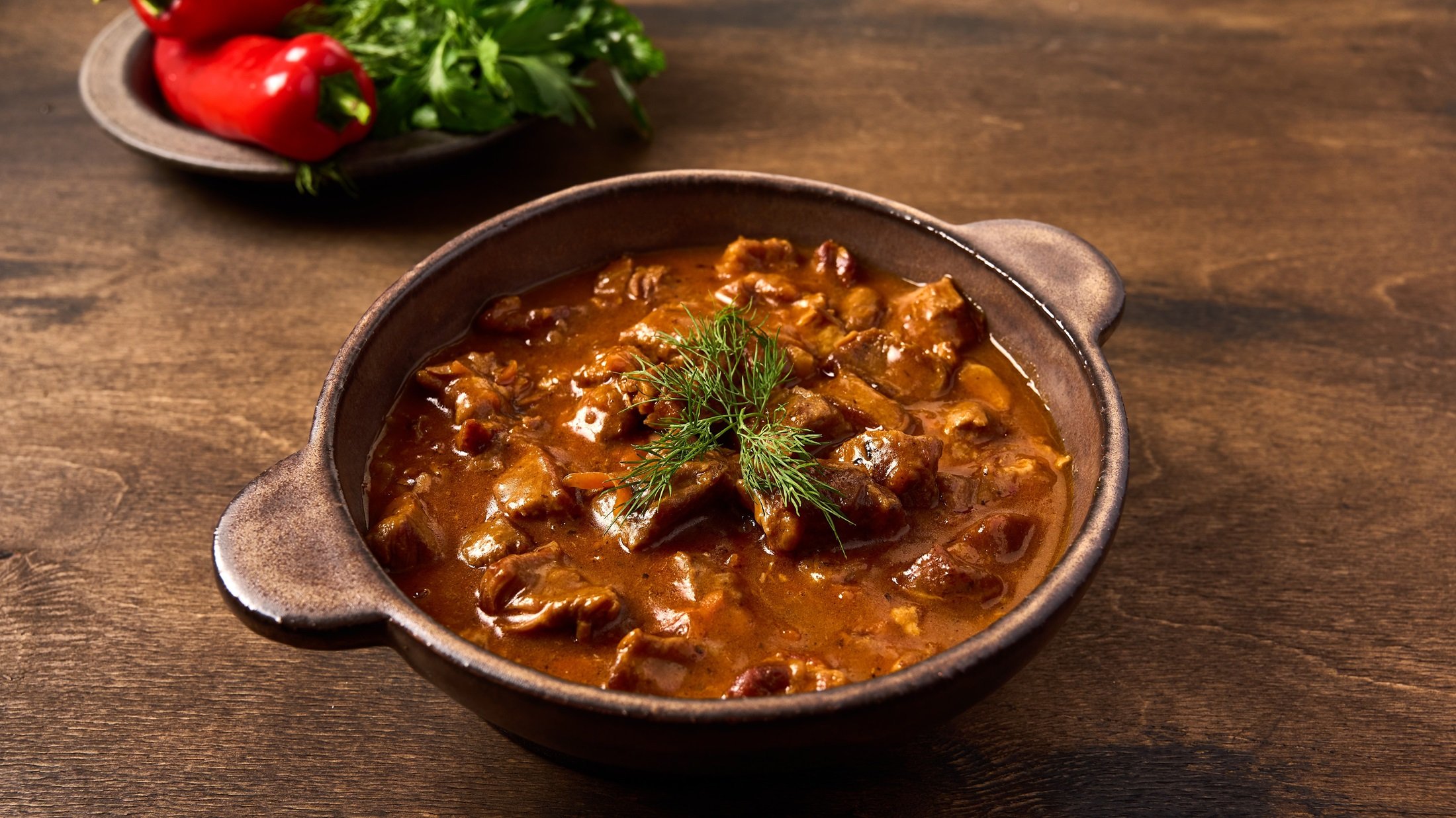 Draufsicht, schräg: Ein Topf Pfefferpotthast, eine Art Pfeffer-Ragout, auf einem Holztisch.