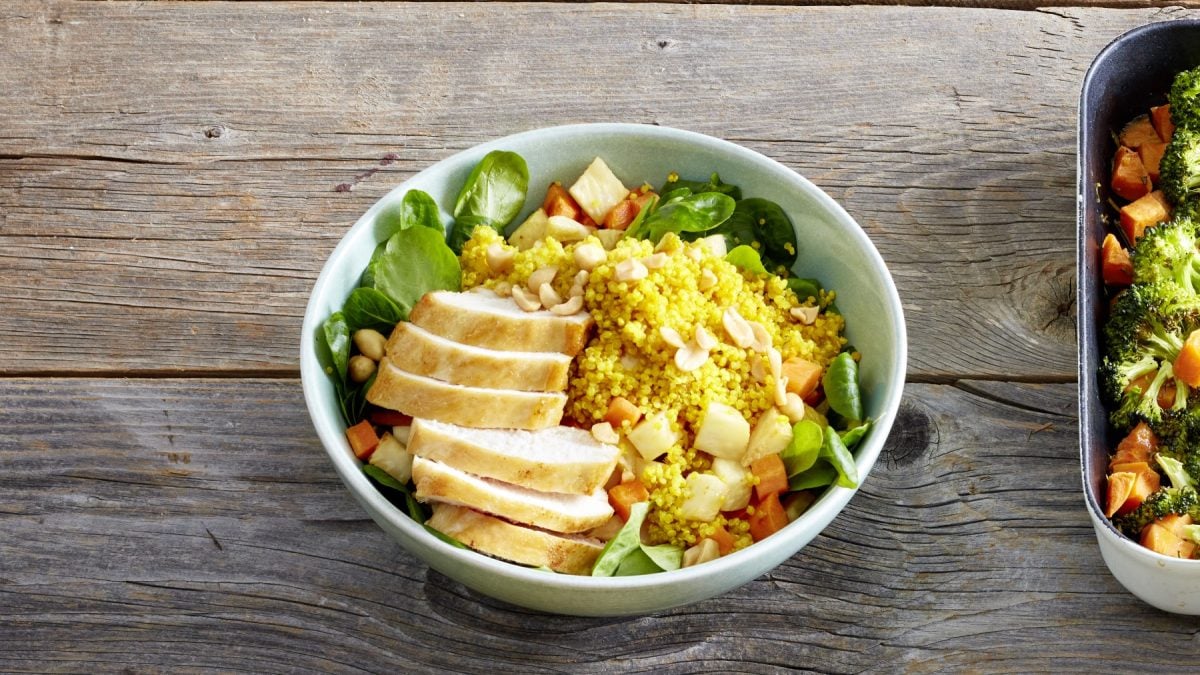 Quinoa-Hähnchen-Bowl in einer Schüssel auf hölzernem Hintergrund.