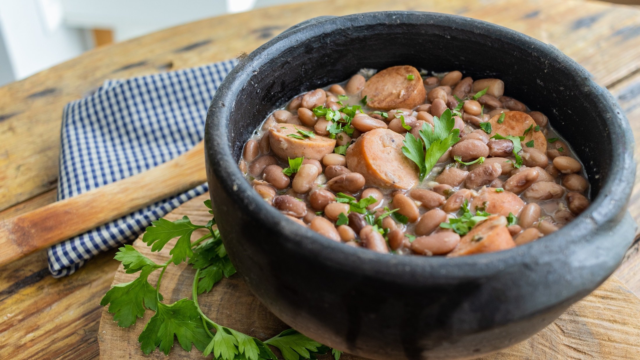 Draufsicht, schräg: veganer Bohneneintopf mit Borlotti-Bohnen und frischer Petersilie in einer schwarzen Schüssel auf einem Untergrund aus Holz.