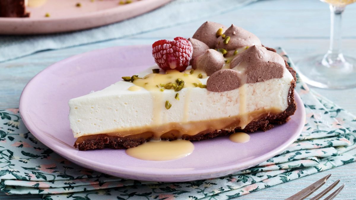 Ein Stück Karamell-Eierlikör-Tarte mit TK-Himbeeren, Pistazienkernen und Eierlikör auf einem rosa Teller.