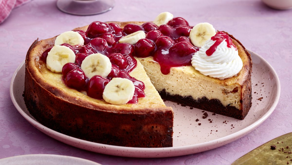 Angeschnittener KiBa-Cheesecake auf rundem Teller mit rosa Hintergrund.