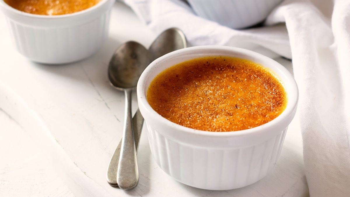 Zwei weiße Schalen mit der Kürbis Crème brûlée auf einem hellen Tisch von schräg oben fotografiert.