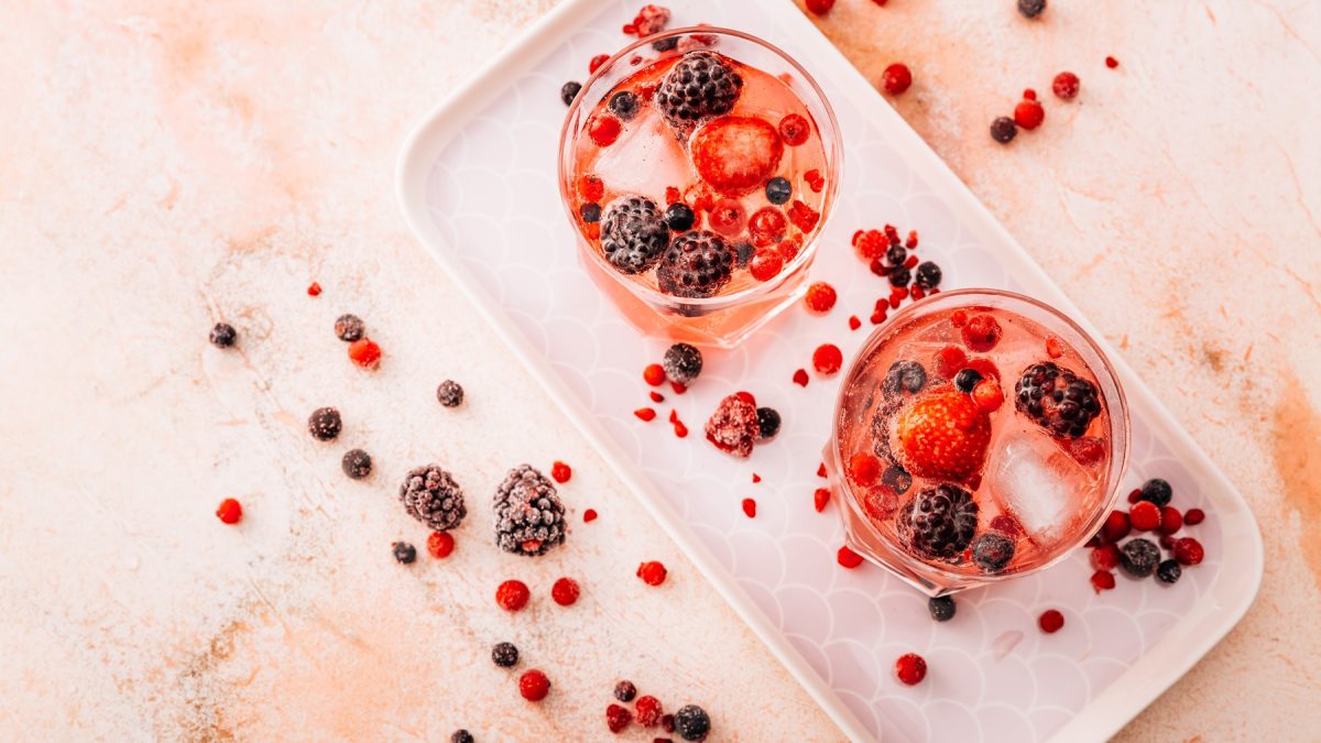 Zwei Gläser mit rosa Lillet Wild Berry, garniert mit Erdbeeren, Brombeeren und roten Johannisbeeren, auf hellem Tablett.