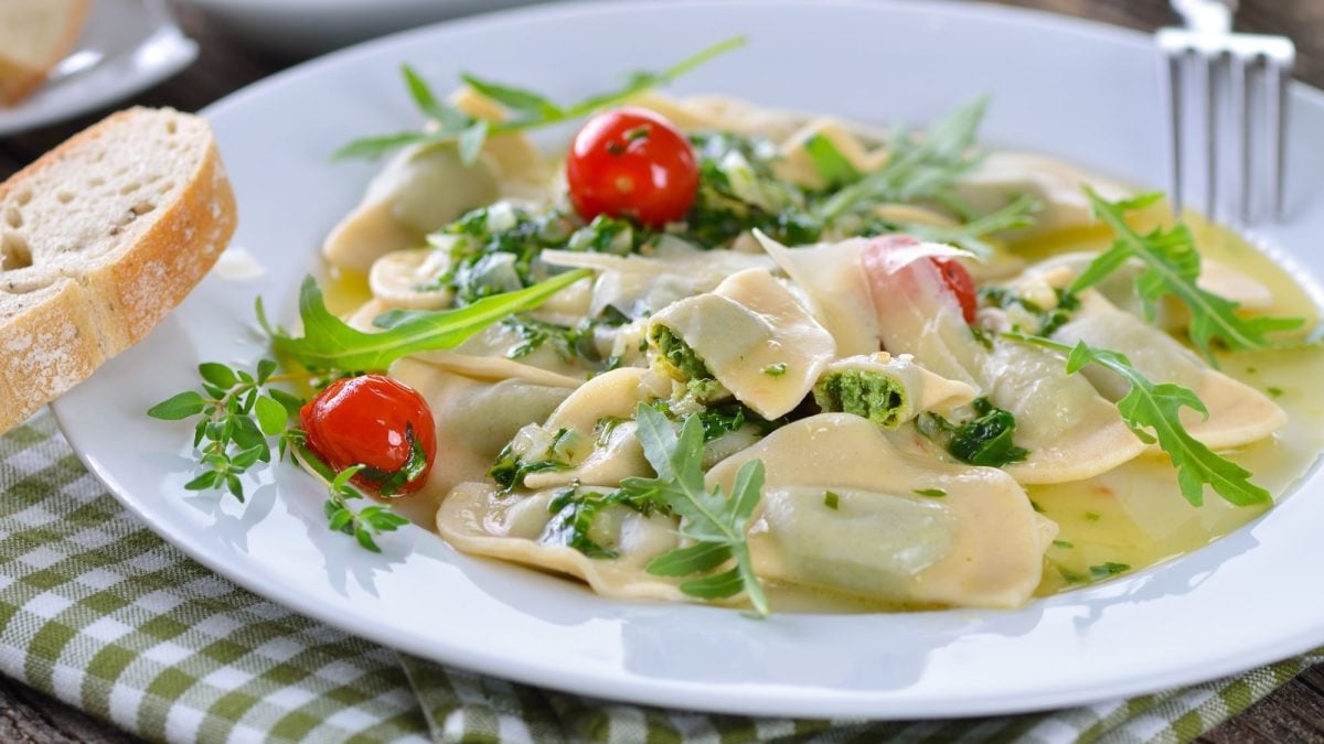 Frische Mezzelune mit grüner Spinatfüllung, serviert in einer leichten Sauce, garniert mit Rucola und Kirschtomaten.