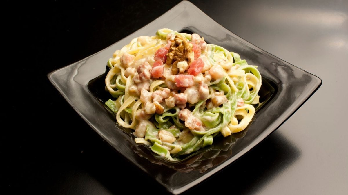 Paglia e fieno – zweifarbige Pasta mit Pancetta und Walnüssen auf schwarzem Teller, edel angerichtet mit einer cremigen Sauce.