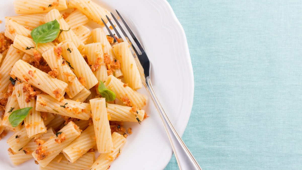 Rigatoni mit Pangritata bestreut auf weißem Teller.