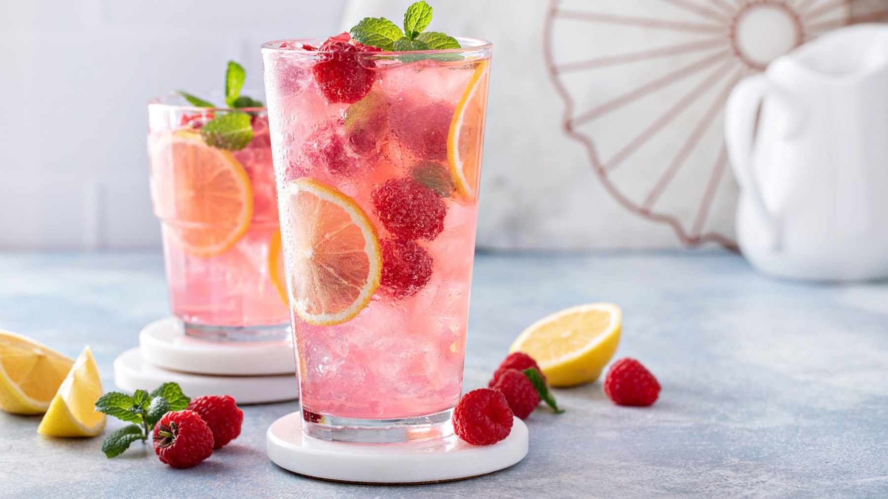 Nahaufnahme eines Glases Raspberry Limoncello mit frischen Himbeeren, Zitronenscheiben und Minzblättern, arrangiert auf einem sommerlichen Tisch.