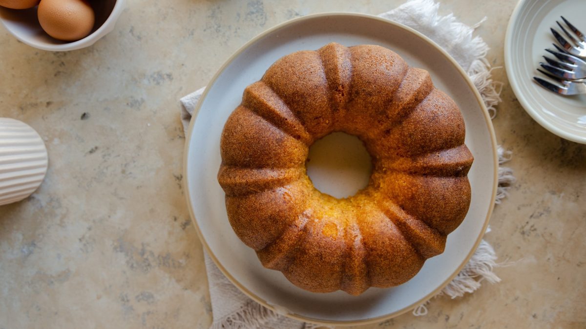 Der Rührkuchen von oben auf einem hellen Teller mit beigem Untergrund fotografiert.