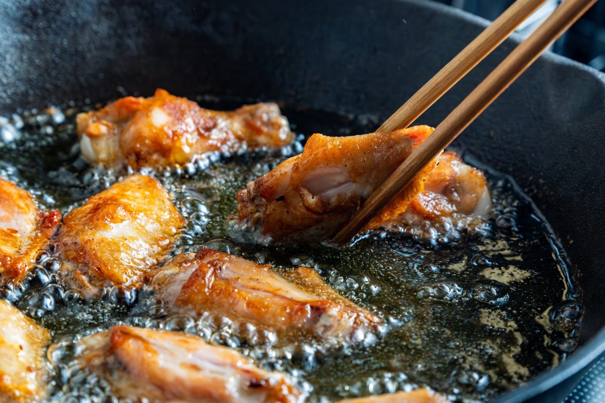 Frittierte Hähnchenflügel, die gerade mit zwei Essstäbchen beim Frittieren gewendet werden. Alles in Nahaufnahme von der Seite.