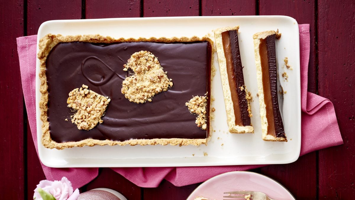 Schoko-Karamell-Tarte auf einem weißen Teller auf dunkelrotem Hintergrund.