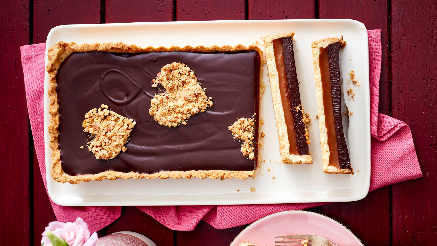 Schoko-Karamell-Tarte auf einem weißen Teller auf dunkelrotem Hintergrund.