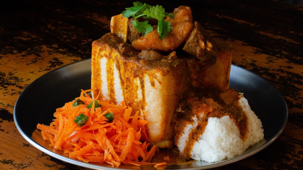 Südafrikanisches Bunny Chow: Ein ausgehöhltes Brot gefüllt mit Curry aus Fleisch und Kartoffeln, garniert mit Koriander, serviert mit scharfem Karottensalat.