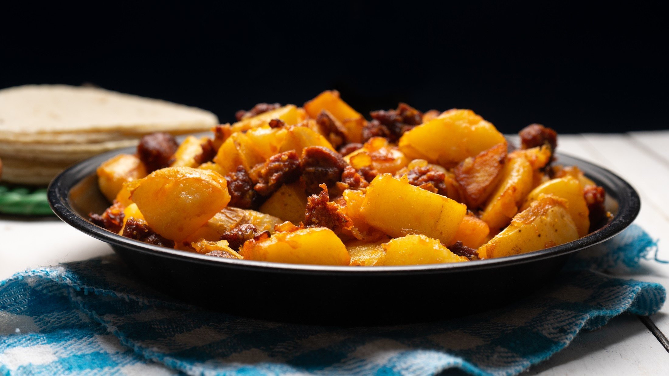 Ein schwarzer Teller mit der Chorizo-Kartoffelpfanne von der Seite fotografiert.