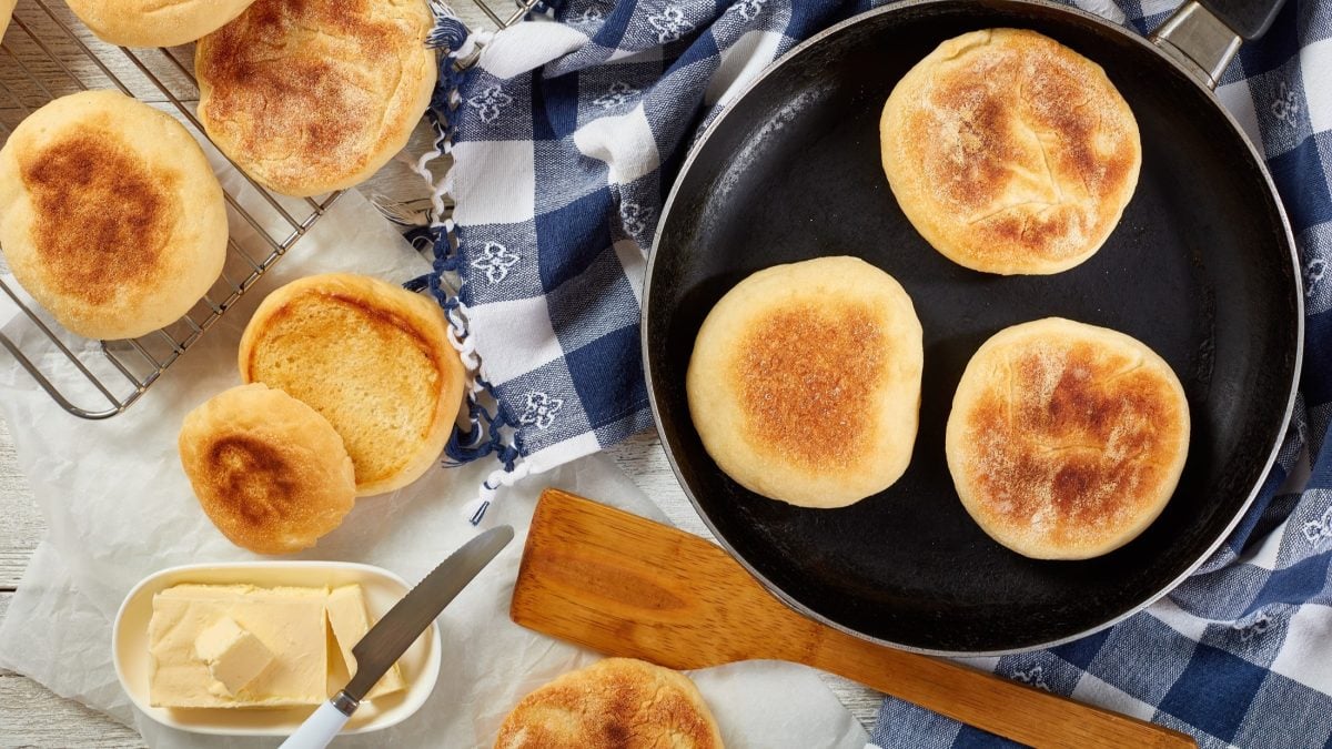 Draufblick: mehrere Toasties aus der Pfanne liegen auf einem hellen Untergrund. Einige English Muffins sind in einer dunklen Pfanne, die anderen liegen daneben.