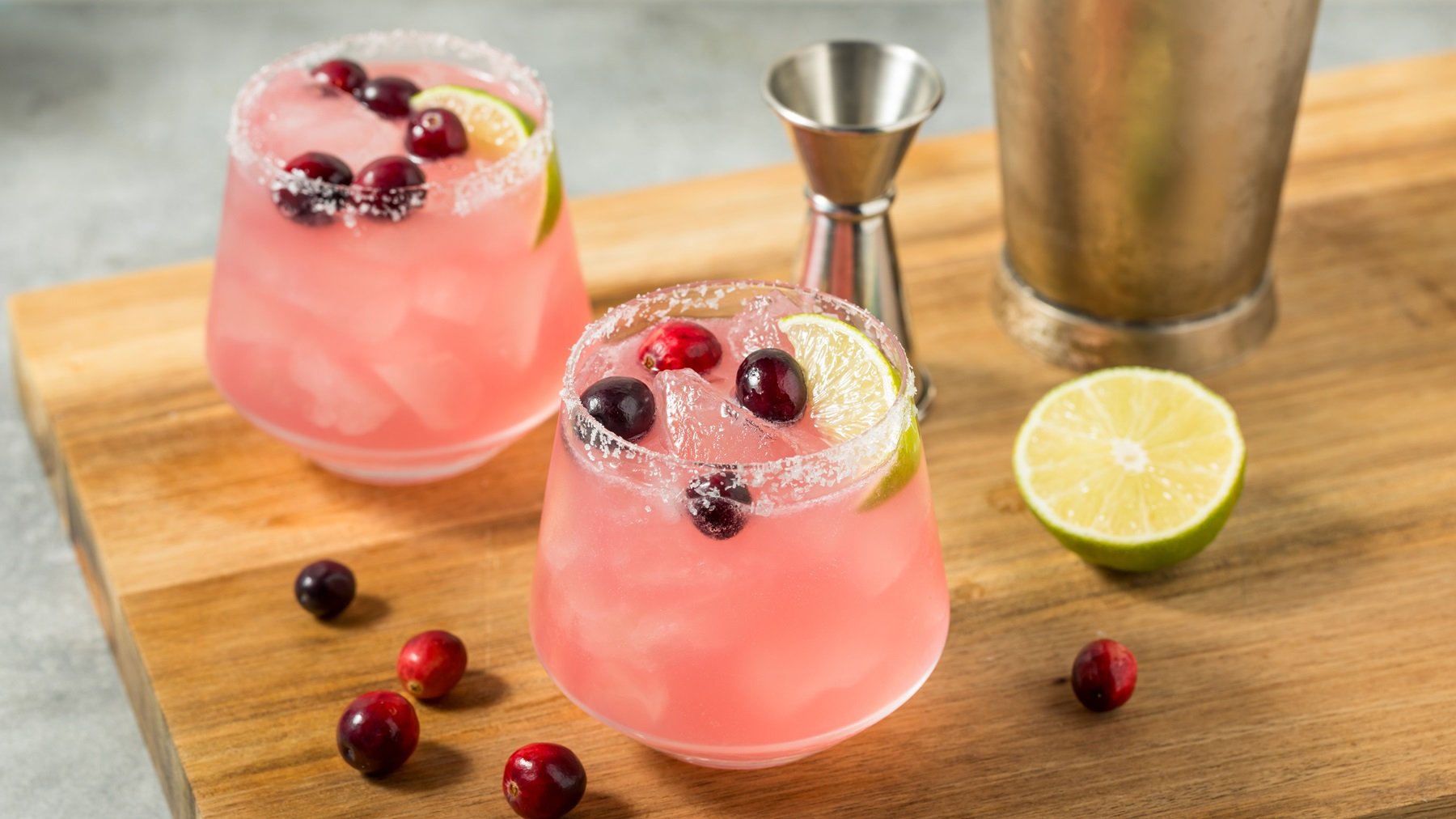 Eisgekühlte Cranberry-Margaritas in Gläsern mit gesalzenem Rand, Cranberrys und Limetten, arrangiert auf einem Holzbrett.