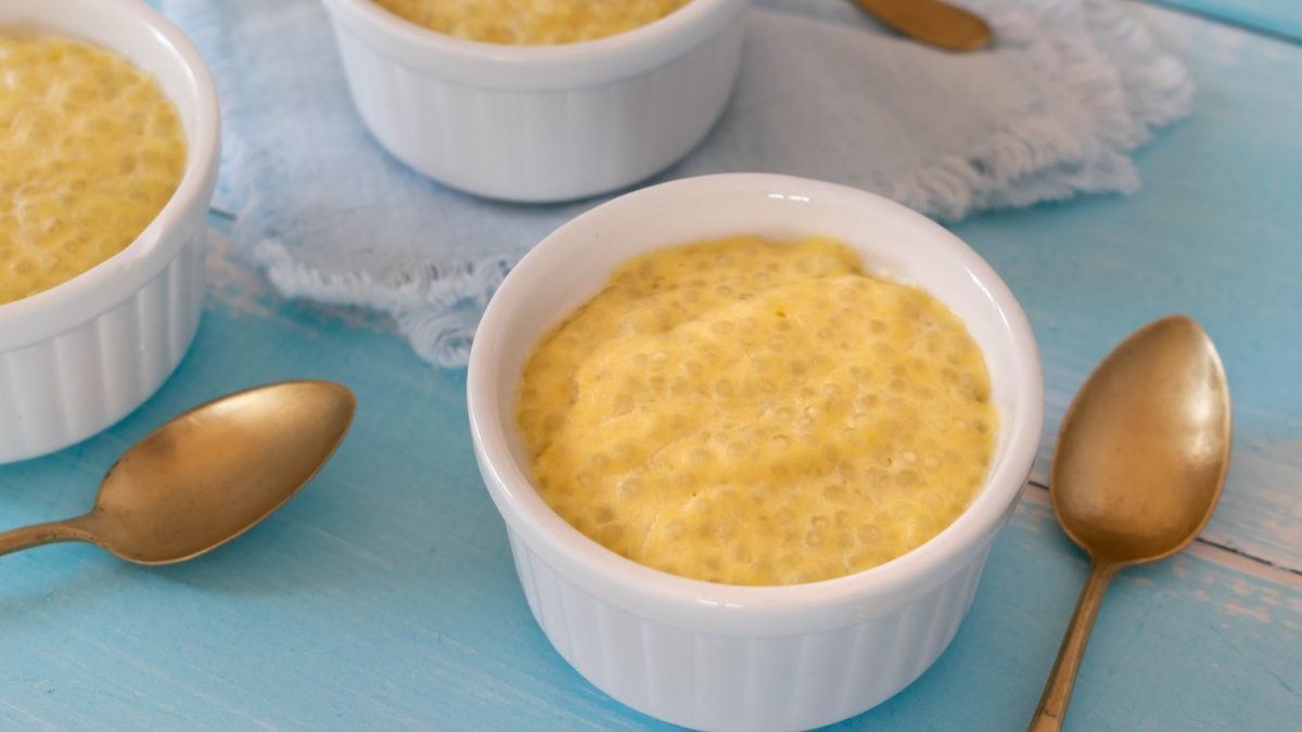 Drei weiße Schälchen mit dem Tapioka Pudding auf einem hellblauen Tisch mit goldenen Löffeln.