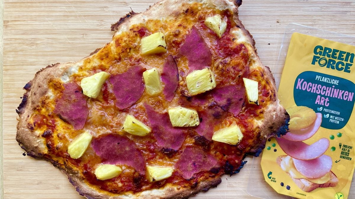 Selbstgemachte vegane Pizza Hawaii mit pflanzlichem Schinken und saftiger Ananas auf hellem Holzuntergrund.