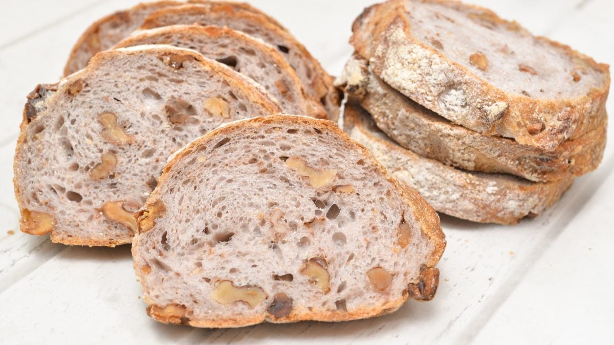 Draufsicht: Weißer Untergrund aus Holz, mehrere Scheiben Walnuss-Baguette.