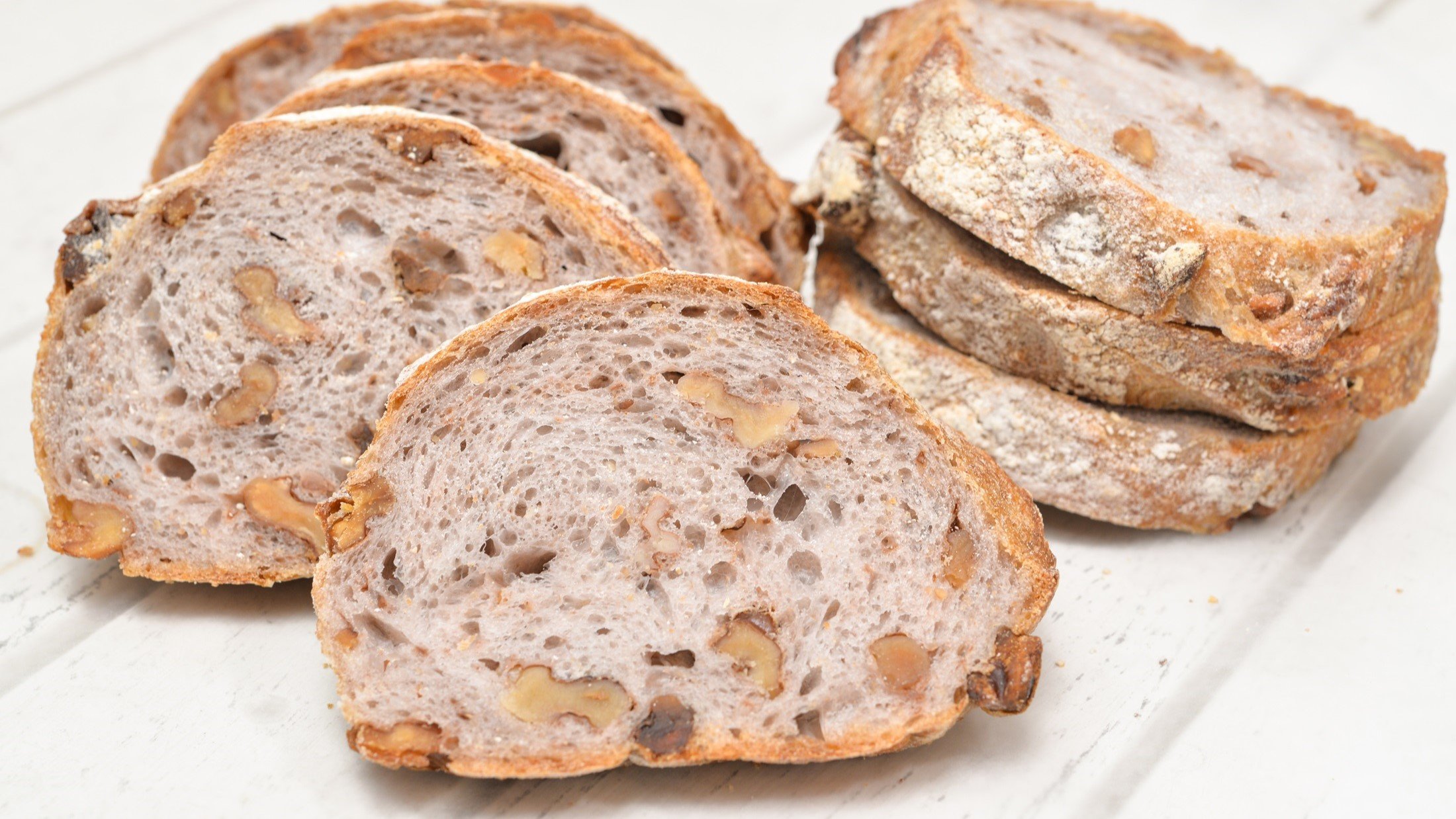 Draufsicht: Weißer Untergrund aus Holz, mehrere Scheiben Walnuss-Baguette.